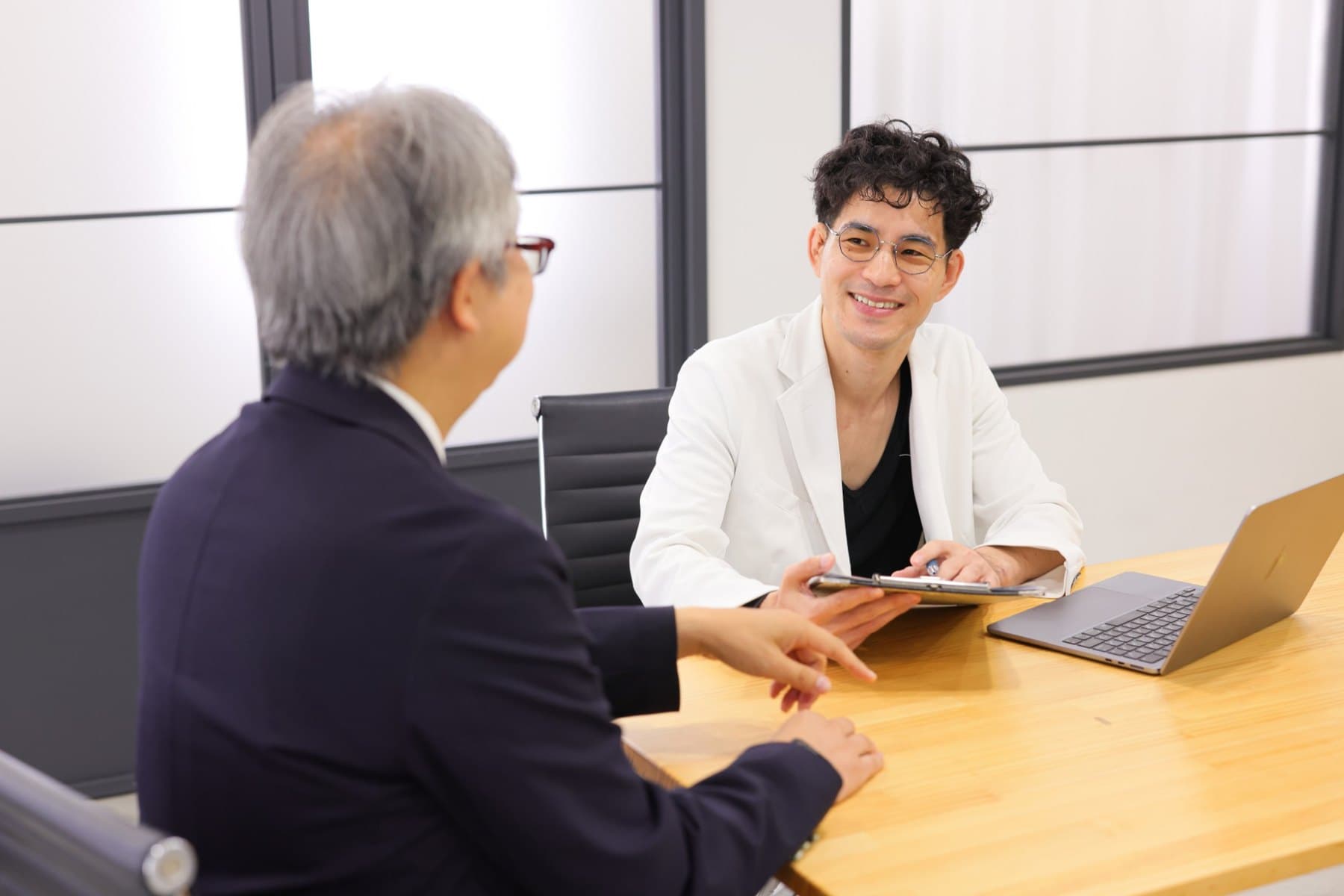白衣の顧問と経営者が、明るい部屋で同じテーブルに向き合う様子